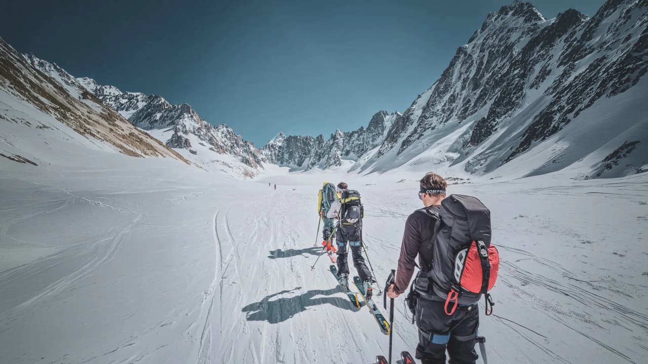 A group of skiers crossing a glacier, surrounded by majestic mountains and brilliant snow.