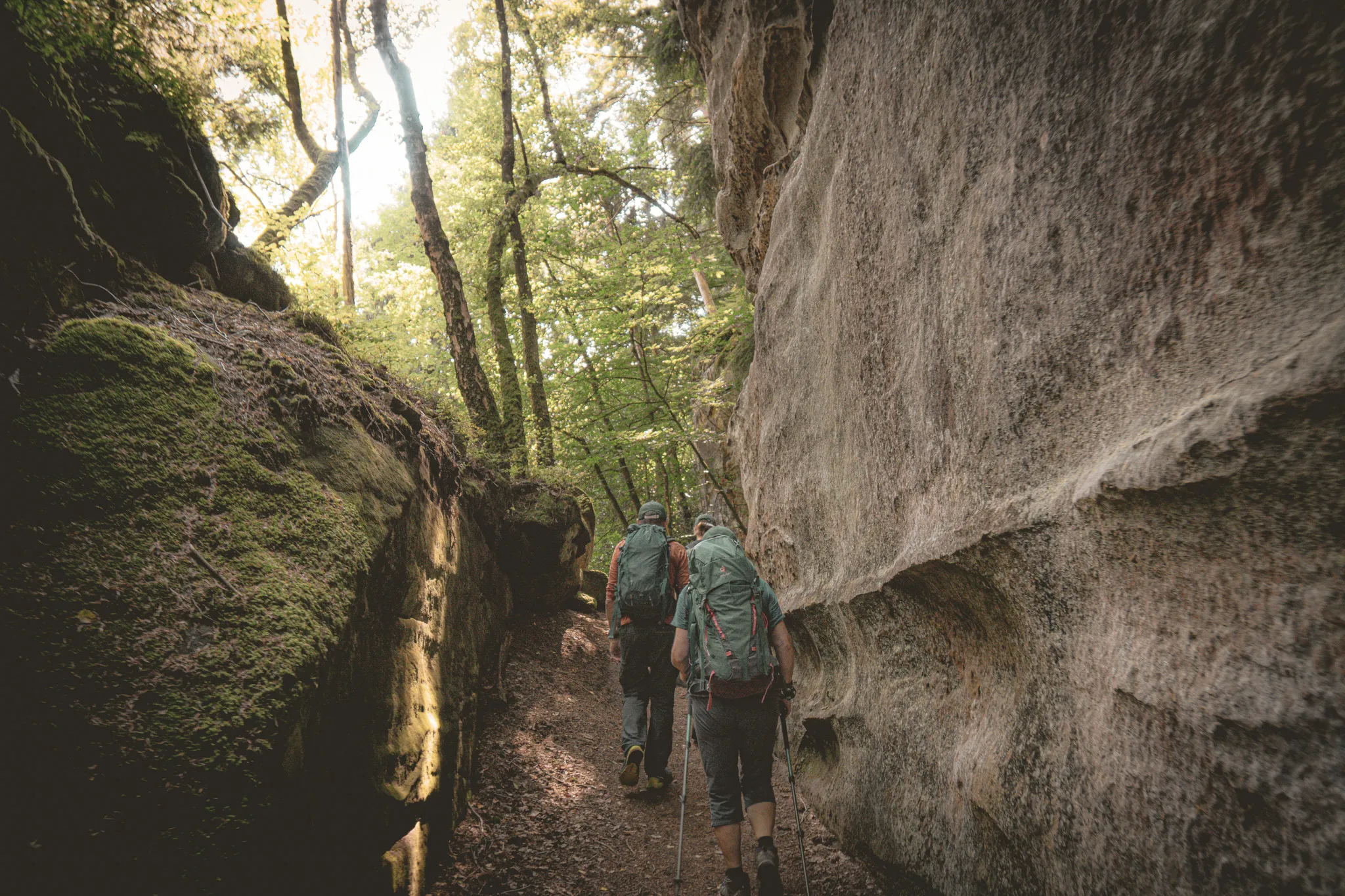 Deux randonneurs avancent sur un sentier escarpé, entourés de rochers et de verdure luxuriante.