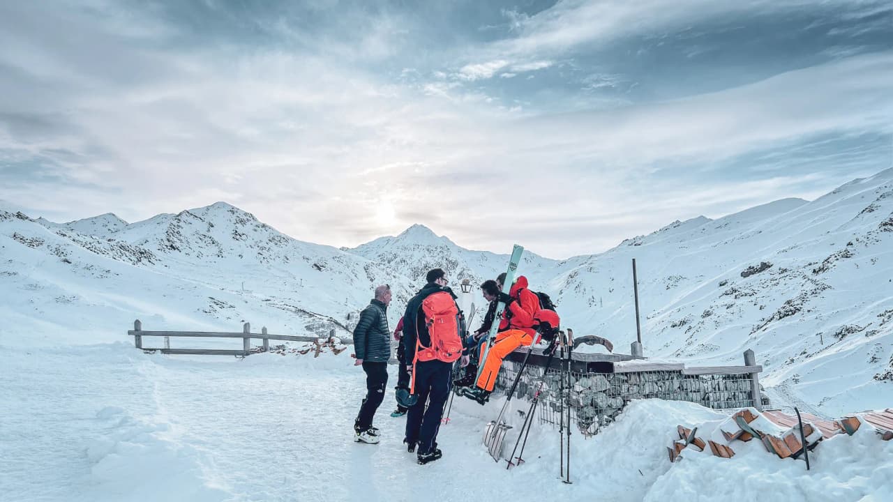 Group of skiers on the Great Saint Bernard Pass, with snow-capped mountains in the background.