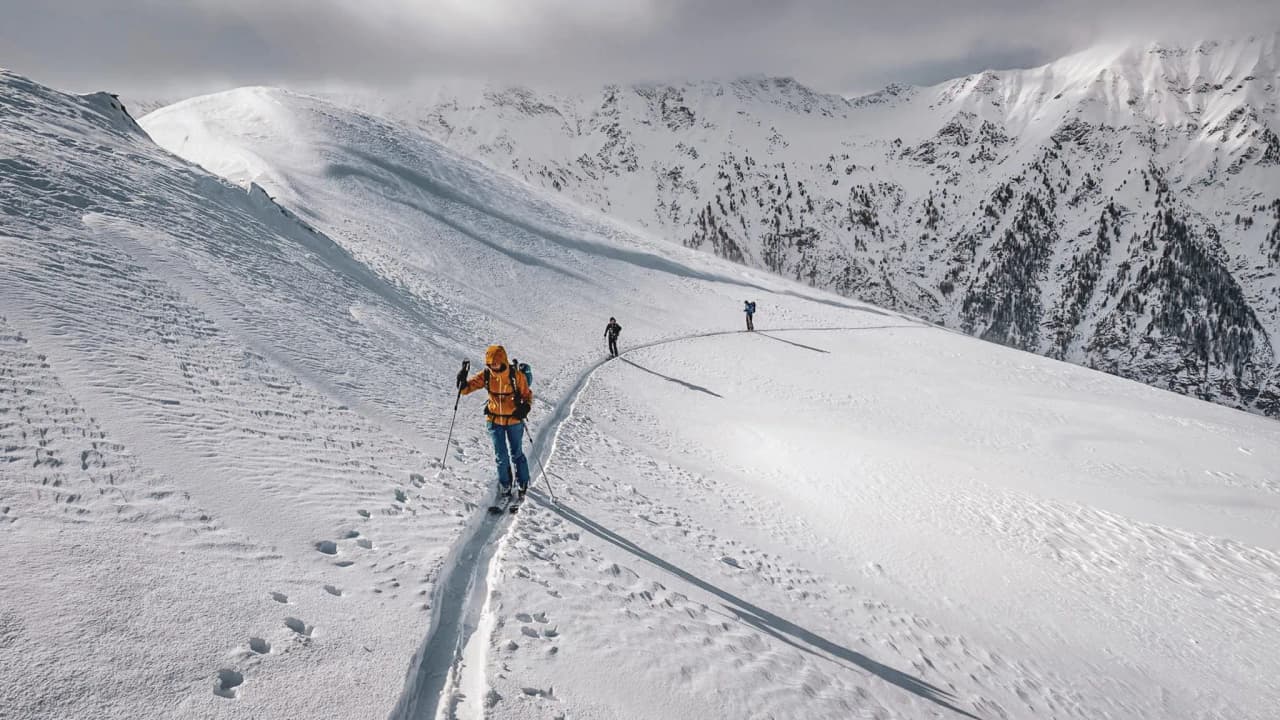 Trois skieurs progressent sur des pentes enneigées, entourés de sommets majestueux du Queyras.