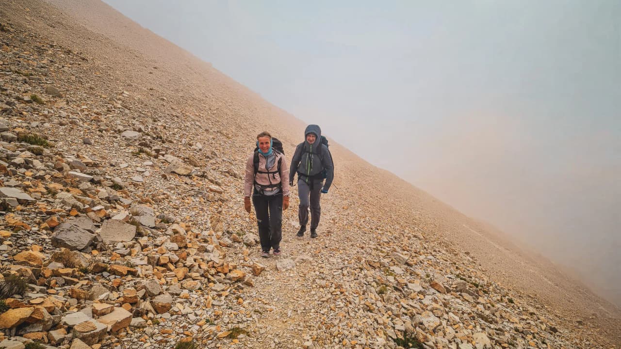 Twee wandelaars lopen over een stenig pad, omringd door mistige alpenlandschappen in de regio Dévoluy.