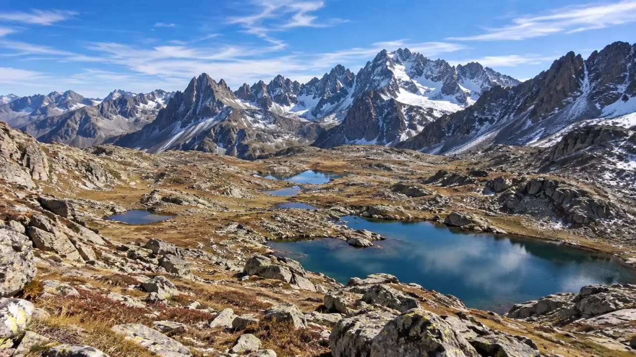 Vastes paysages alpins avec lacs scintillants et sommets majestueux sous un ciel bleu clair.