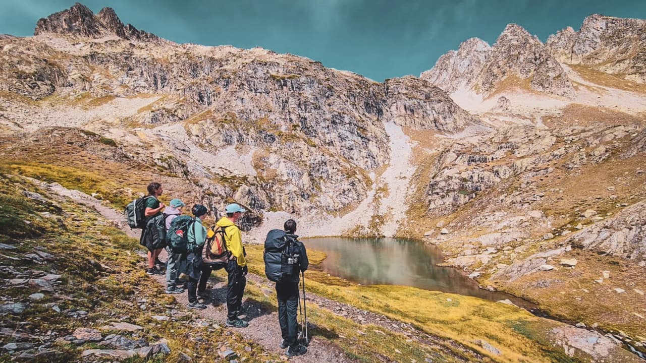 Een groep wandelaars die een bergmeer in de Hoge Pyreneeën bewondert, majestueuze landschappen.
