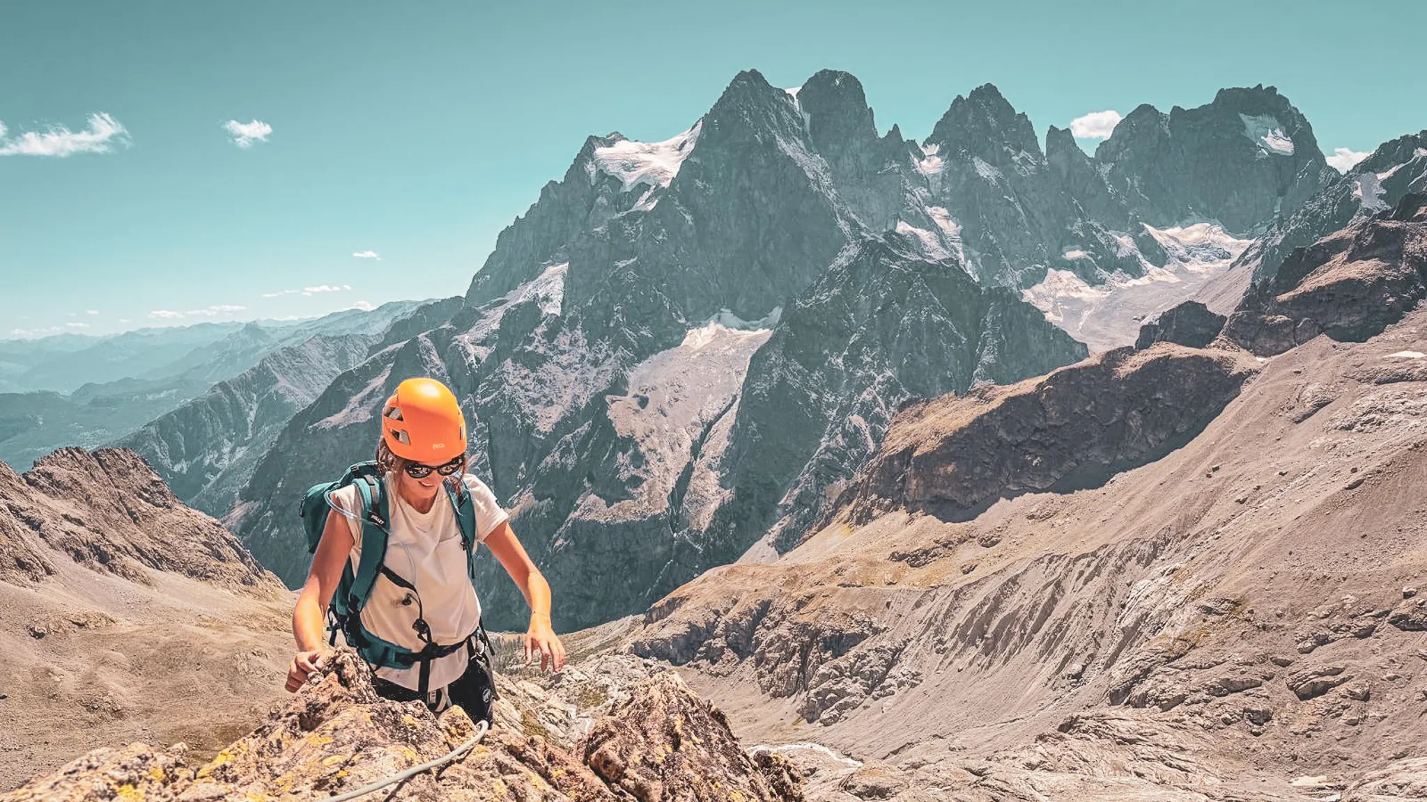 Alpiniste grimpant sur un sommet des Écrins, avec des montagnes majestueuses en arrière-plan.