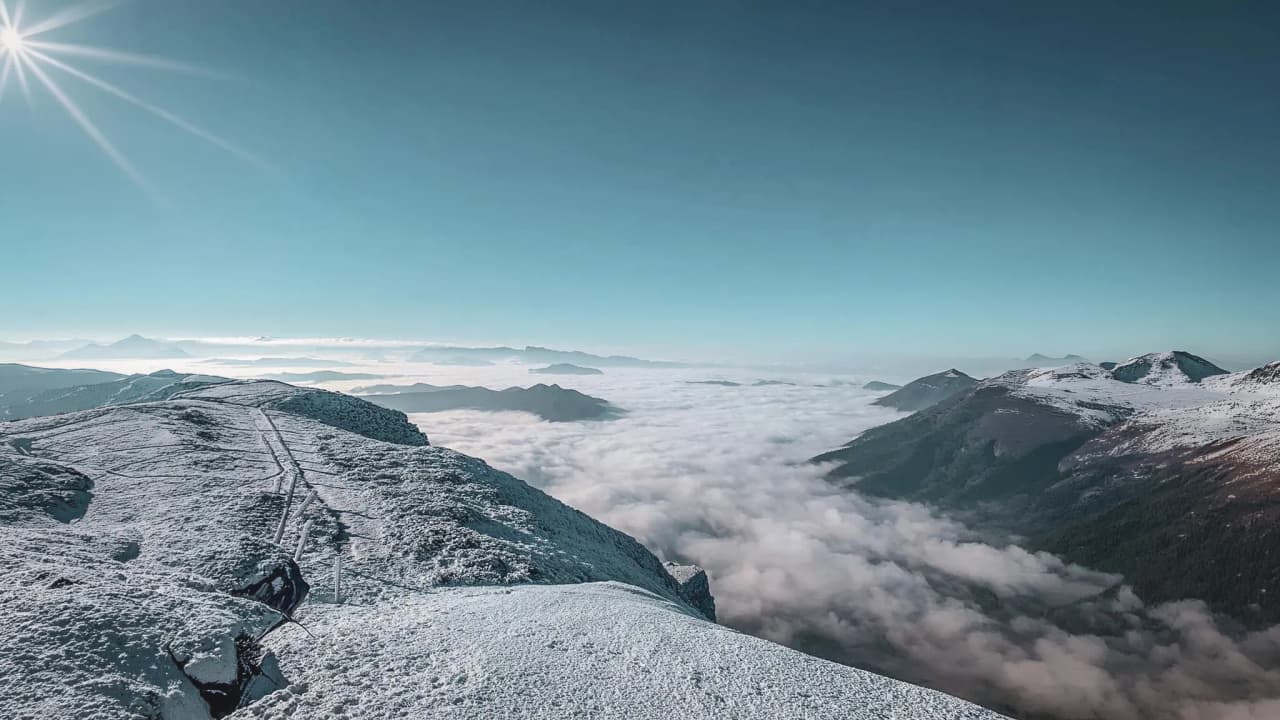 Panorama montagneux sous un ciel bleu éclatant, enveloppé de nuages. Évasion hivernale assurée !