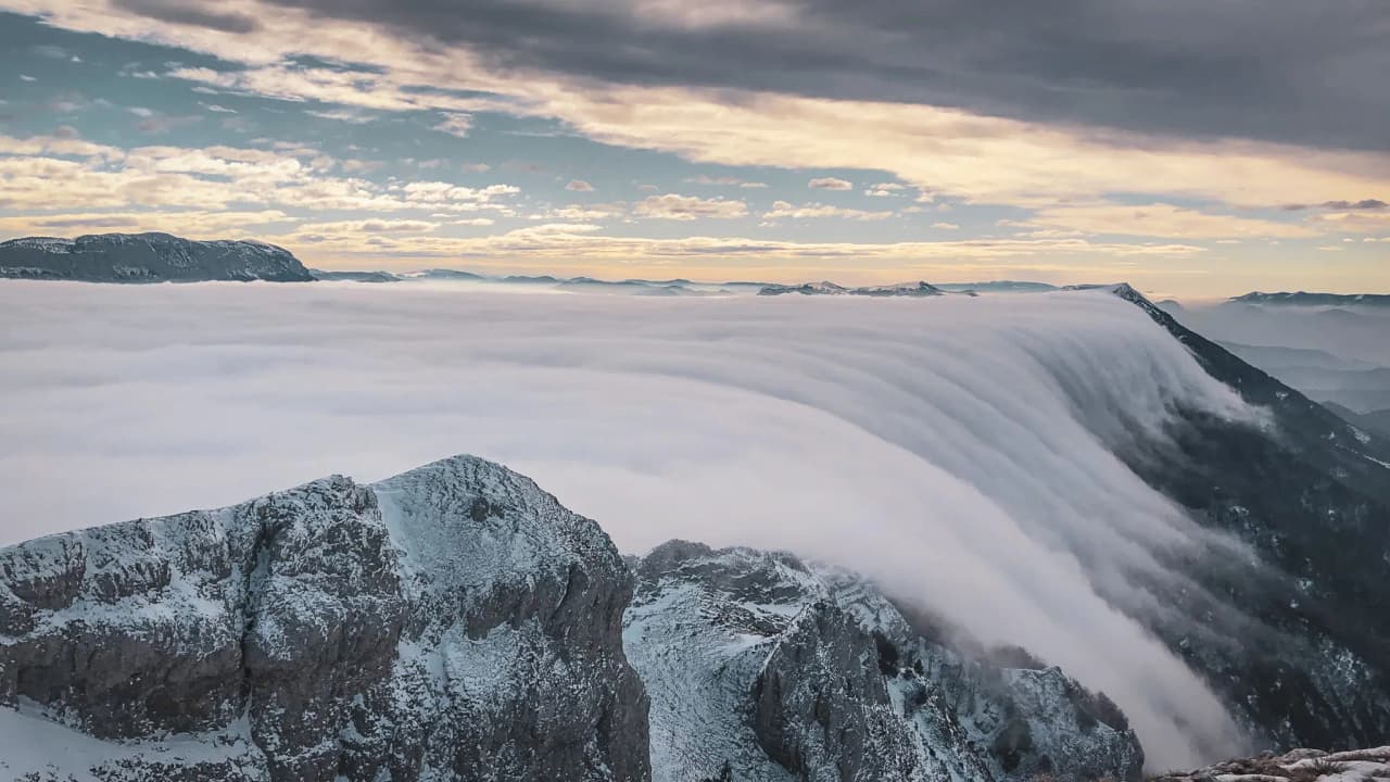 Vue panoramique des montagnes du Vercors, enveloppées de nuages et de neige, au crépuscule.