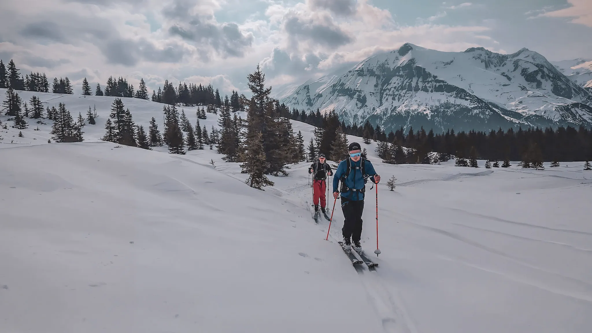 Skiers progress through a snow-covered landscape with majestic mountains in the background.