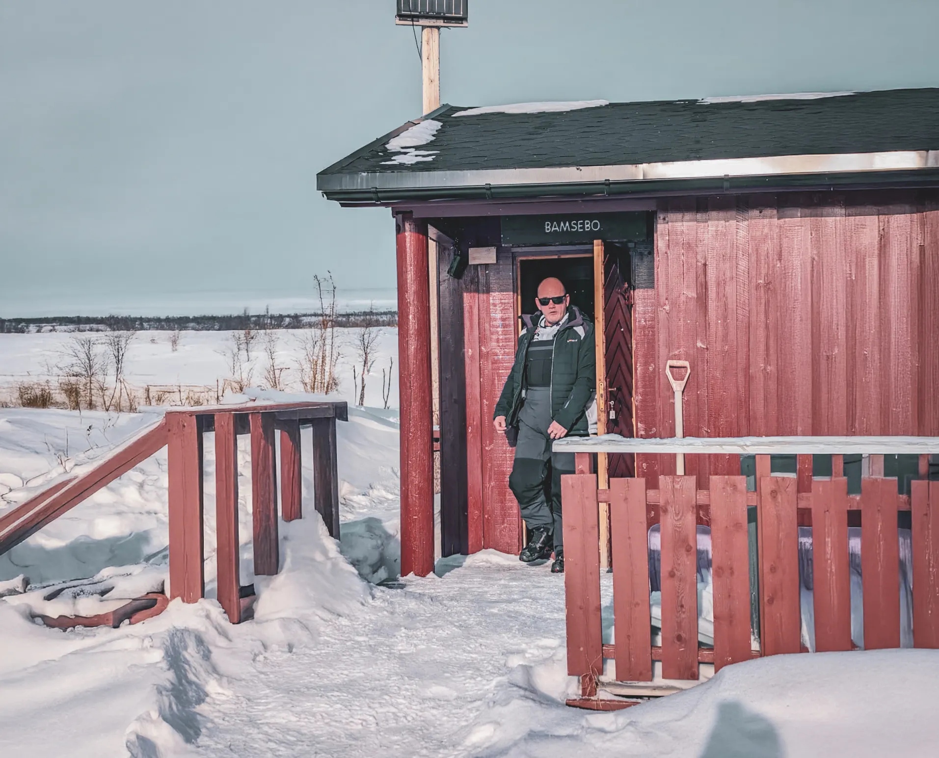 Man in the sun in front of a snow-covered Mountain hut, ready for an adventure in Norwegian Lapland.