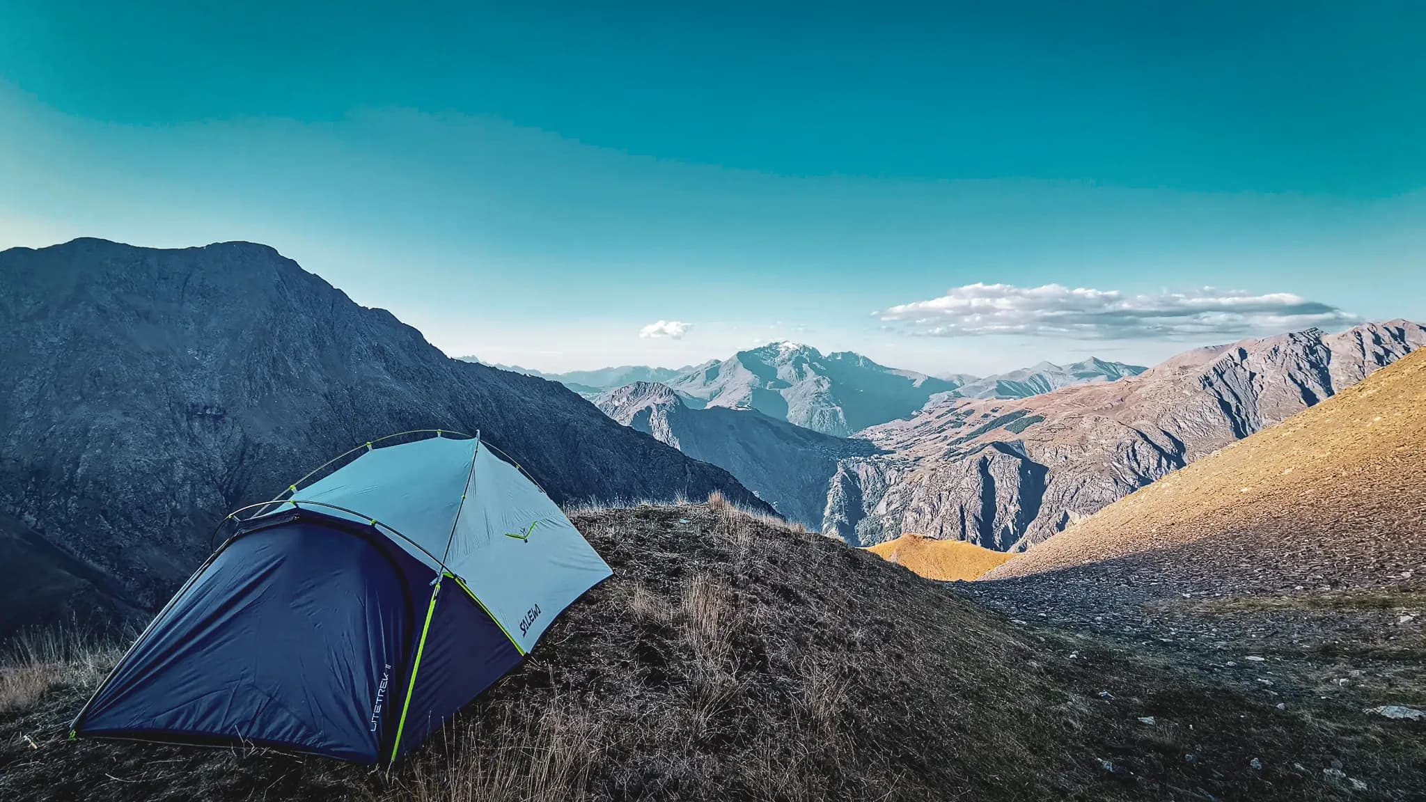 Tente colorée sur un sommet escarpé avec un panorama spectaculaire des montagnes environnantes.