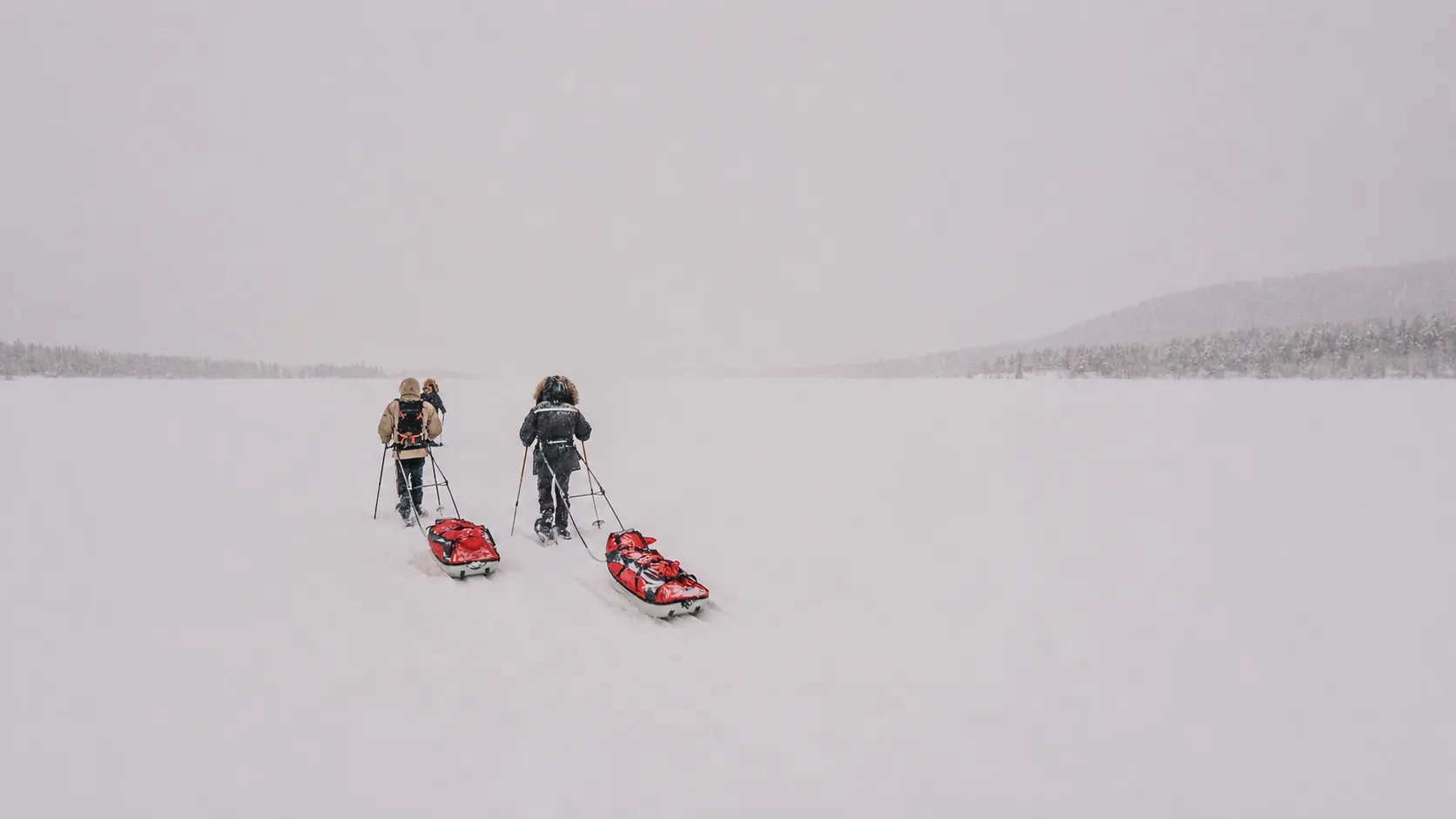 Drie avonturiers op sneeuwschoenen trekken pulka's door een uitgestrekt besneeuwd landschap in Lapland.