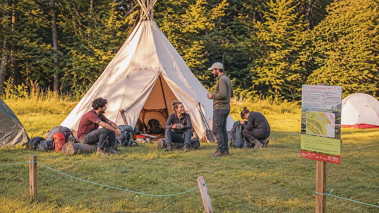 Groupe de randonneurs autour d'une tente, profitant de la nature verdoyante et du bivouac.