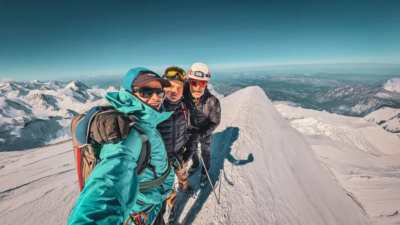 Three mountaineers pose on the summit of Mont Blanc, surrounded by majestic snow-covered landscapes.