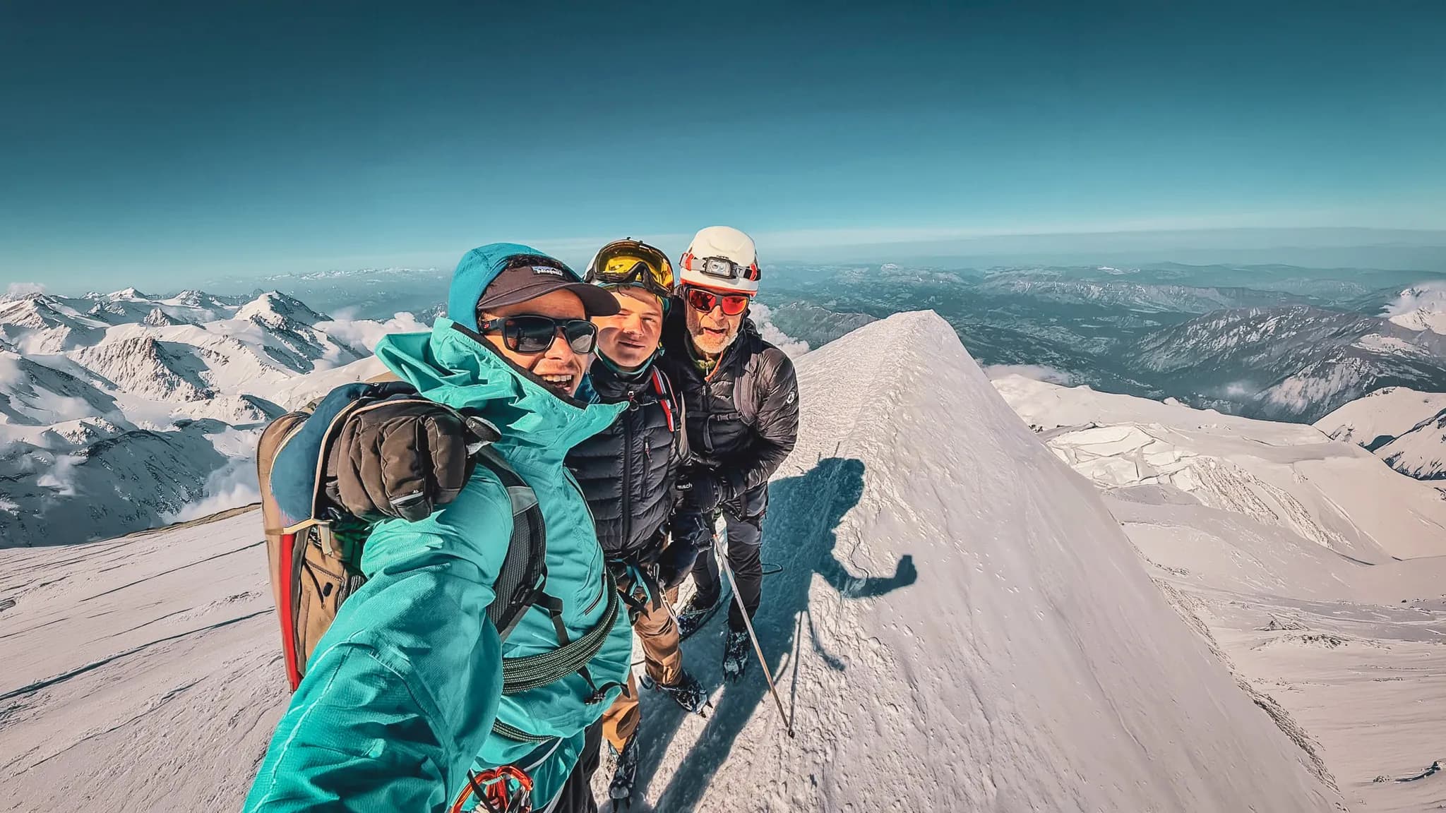 Trois alpinistes posent au sommet du Mont Blanc, entourés de paysages majestueux enneigés.