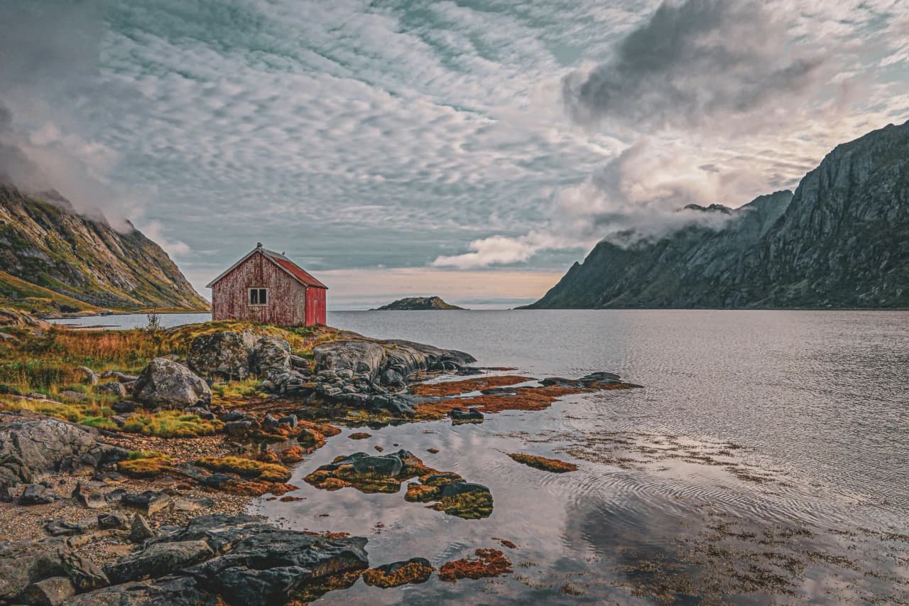 A red cabin on the edge of a fjord, surrounded by majestic mountains, in the peaceful atmosphere of Lofoten.