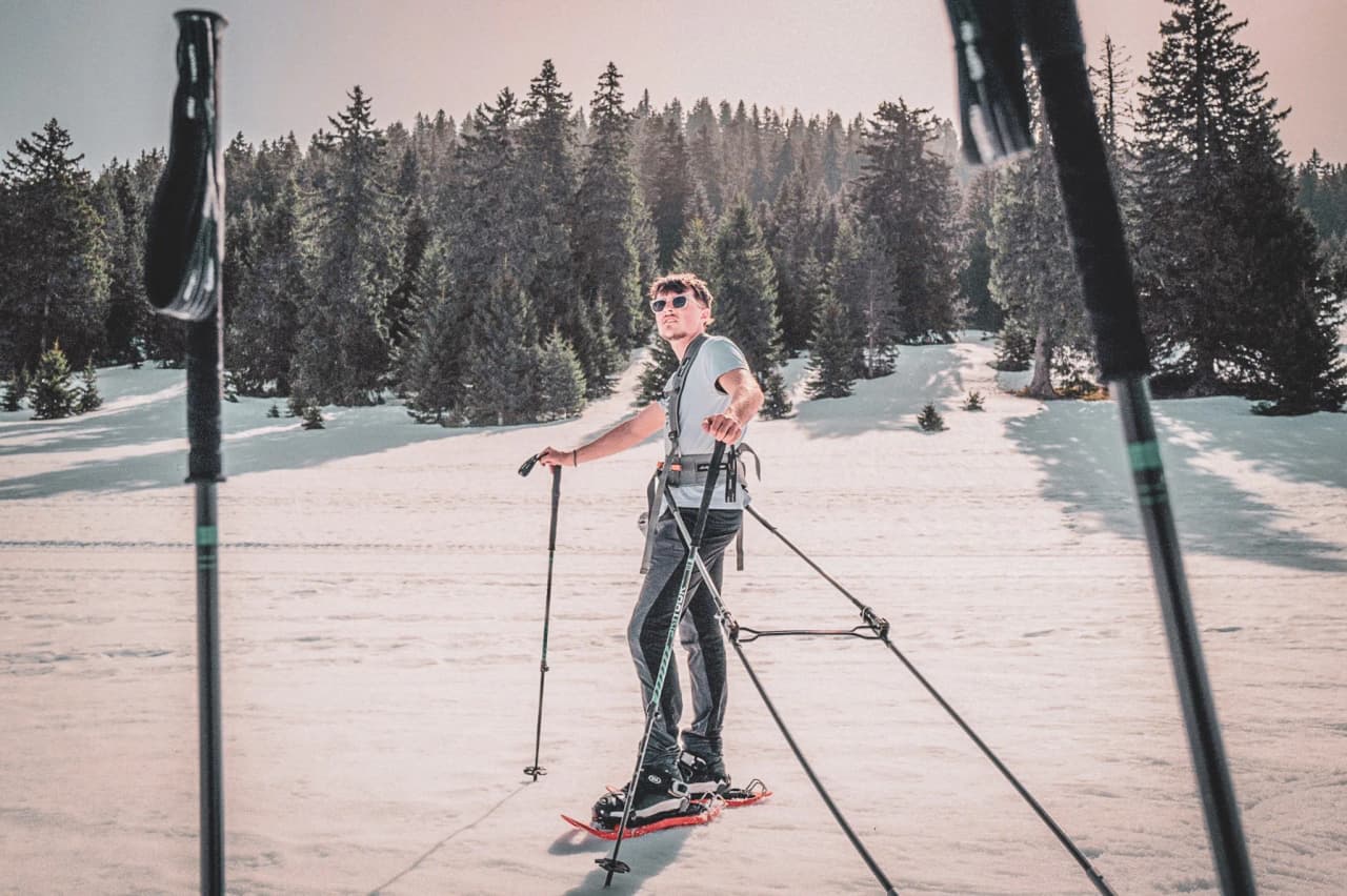 A man on snowshoes on a snow-covered landscape, surrounded by lush green forests. A Nordic escape!