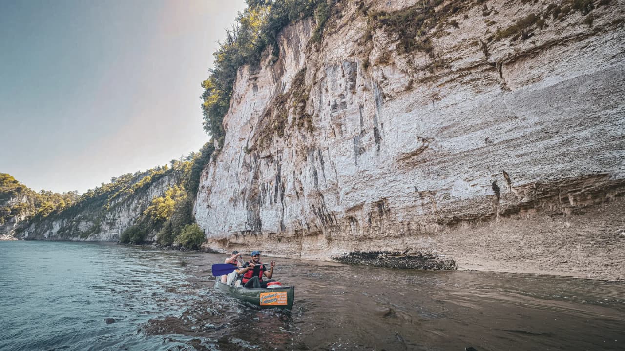 Canoë sur la Dordogne, entouré de falaises blanches majestueuses et d'une nature préservée.