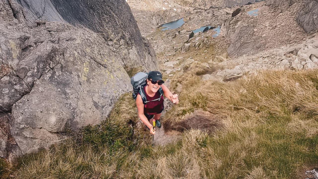 A smiling climber on a mountain trail, surrounded by rocks and lakes in the Pyrenees.