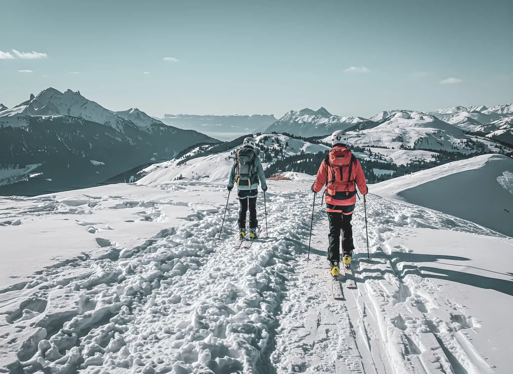 Two ski tourers make their way through a snow-covered alpine landscape, surrounded by majestic mountains.