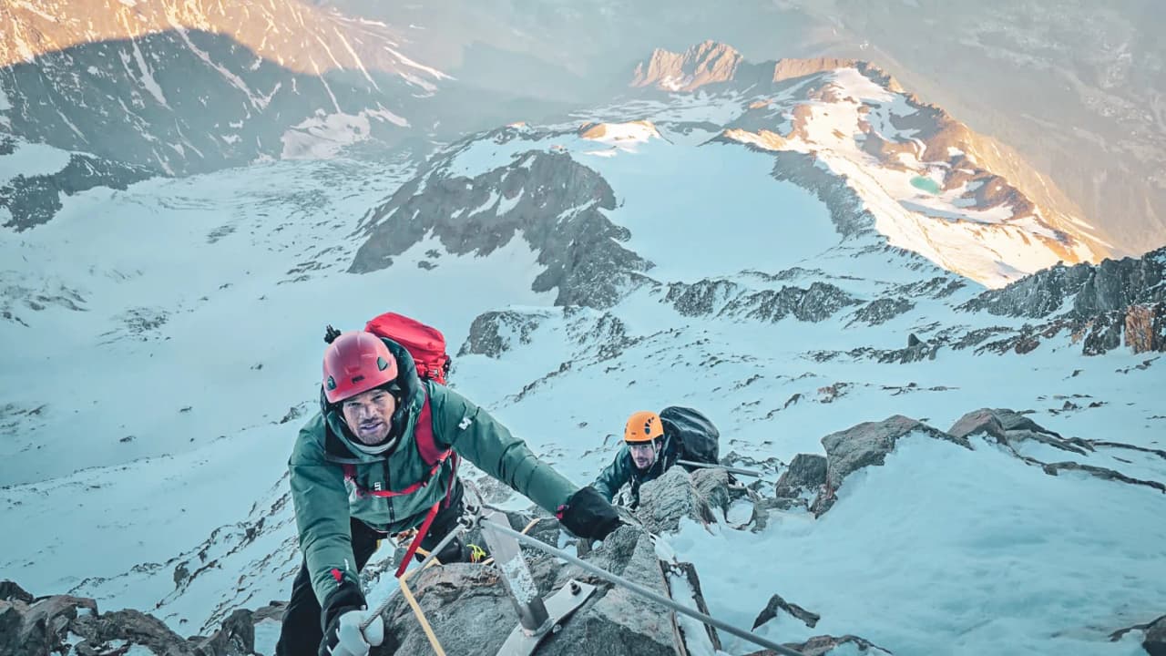 Twee bergbeklimmers beklimmen een besneeuwde helling van de Mont Blanc met een spectaculair uitzicht op de toppen.