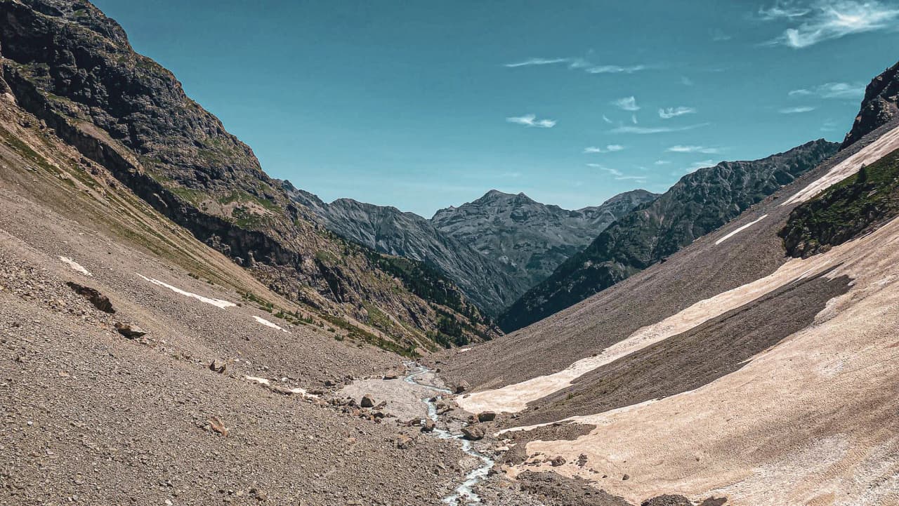 Vallée majestueuse des Écrins, avec des montagnes impressionnantes et un ruisseau sinueux.