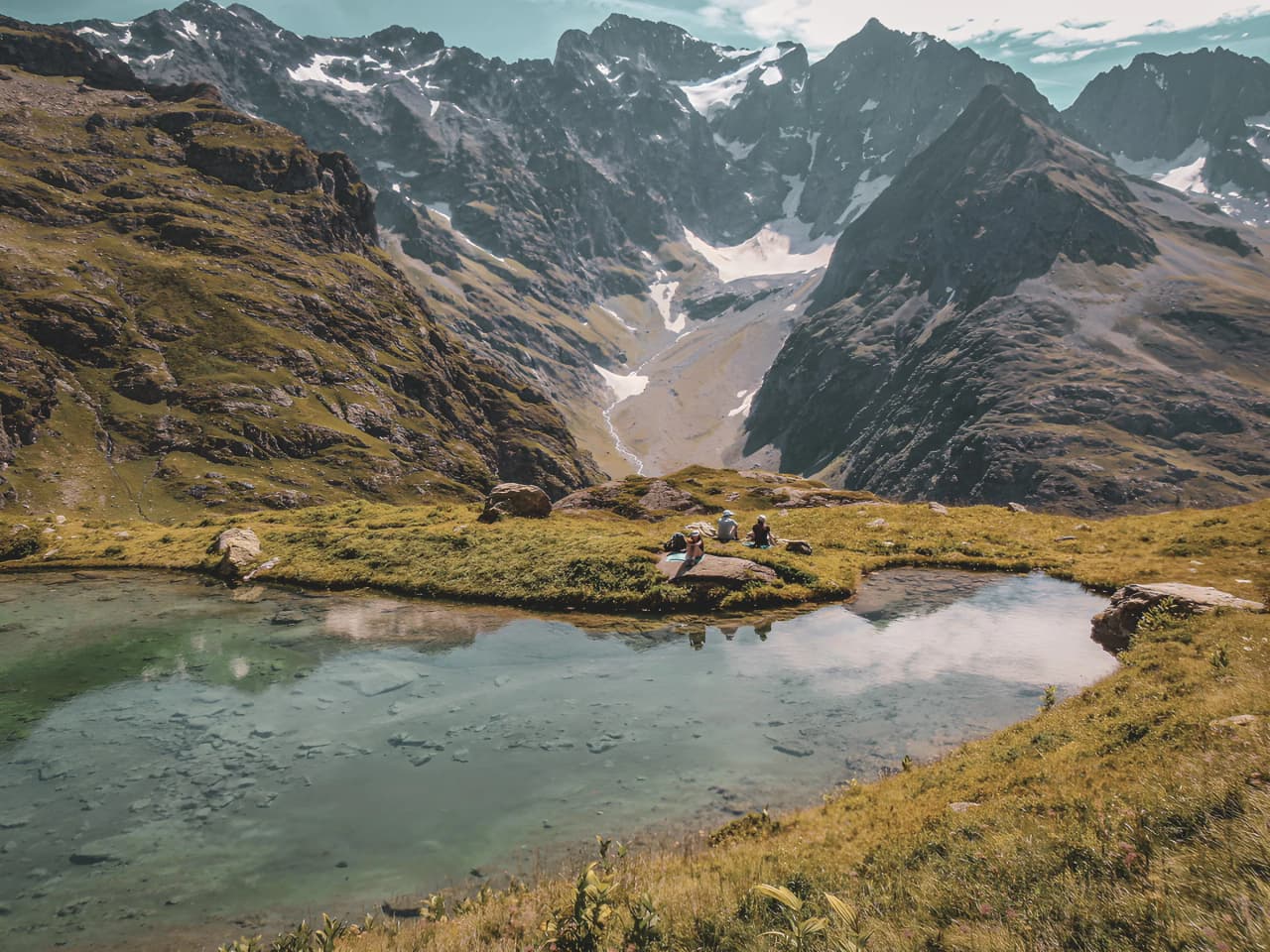 Un groupe de randonneurs se repose au bord d’un lac d'altitude, entouré de montagnes majestueuses.
