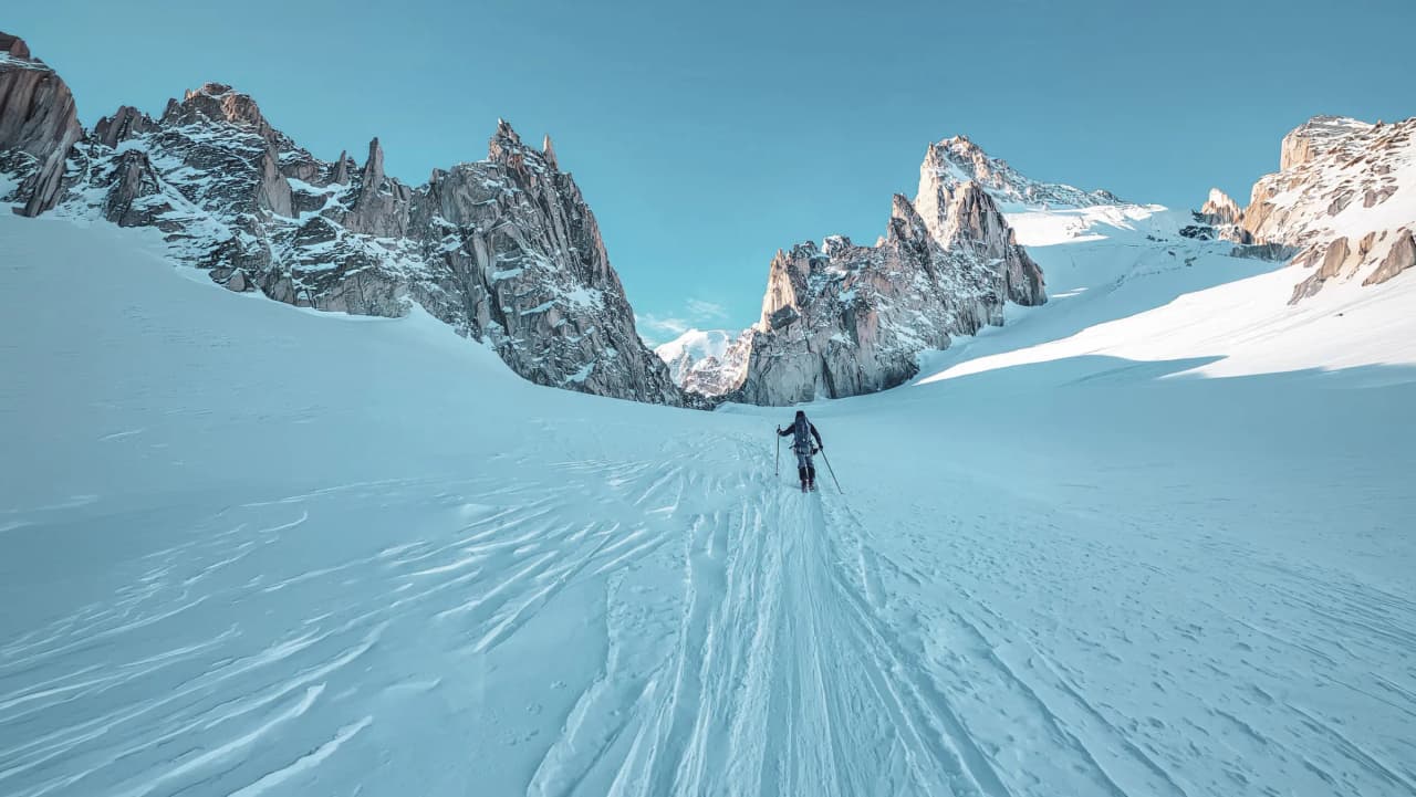 A lone skier on a majestic glacier, surrounded by rocky peaks under a blue sky.