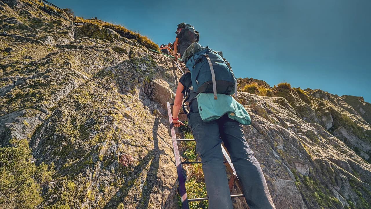 Climb a ladder up a steep rock face, surrounded by breathtaking mountain scenery.
