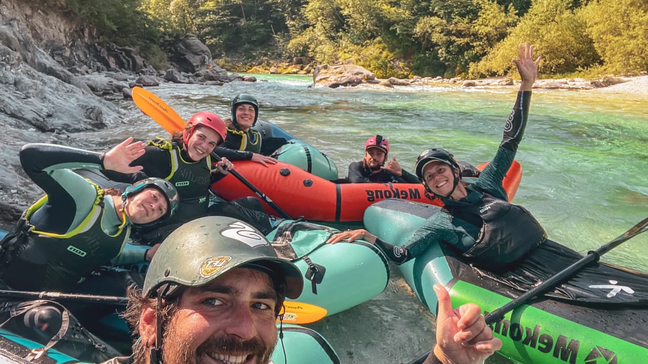 A smiling packraft team on a crystalline alpine river in Slovenia, with an adventurous atmosphere.