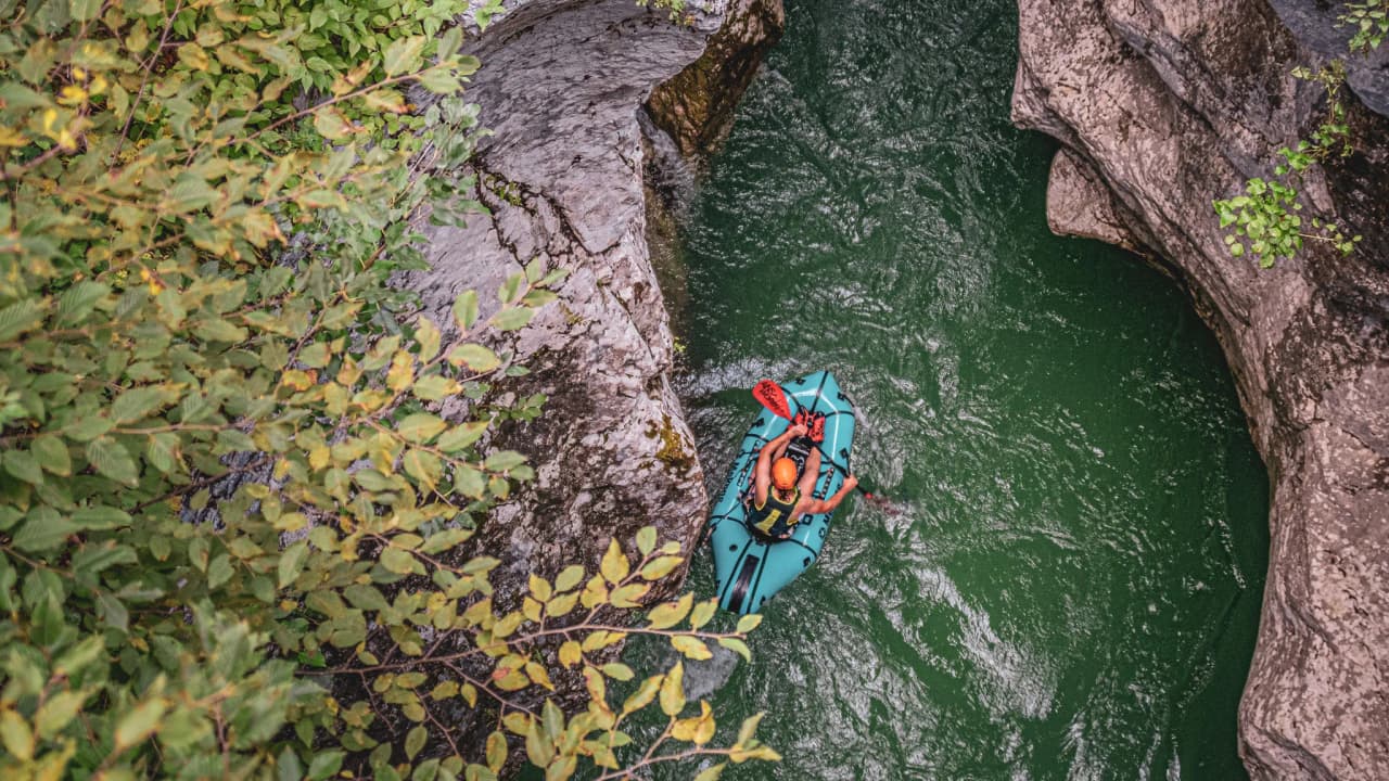 A packraft adventurer navigates an Alpine river surrounded by green cliffs.