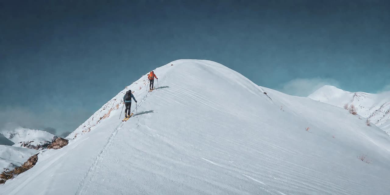 Ski touring in the Ecrins: adventurers on a snow-covered ridge beneath a blue sky.