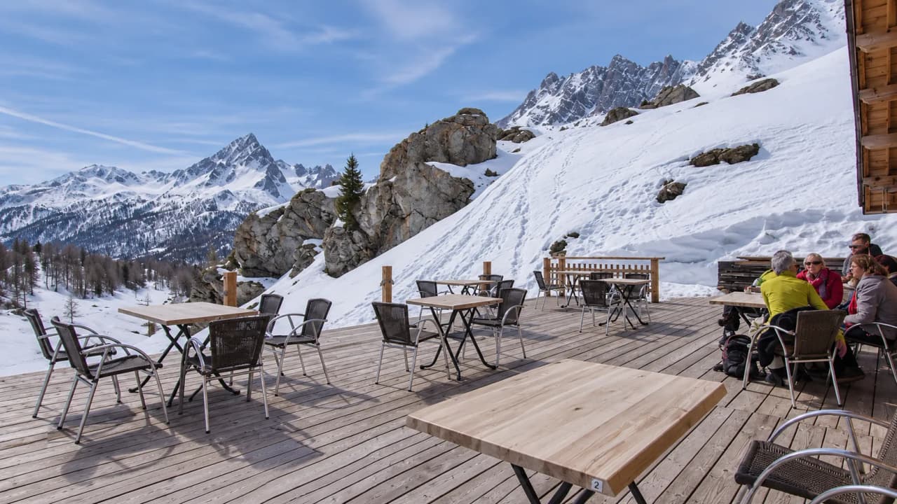 A wooden terrace with a panoramic view of the snow-capped mountains of the Clarée Valley.