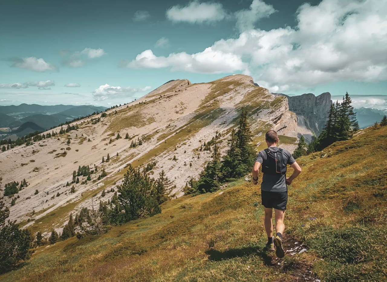 A runner on a lush green trail, with majestic peaks in the background, inspiring a sense of adventure.
