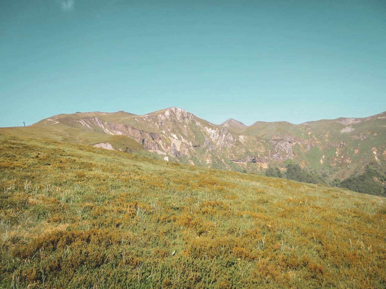 Een uitgestrekt groen landschap van vulkaanruggen in het Centraal Massief onder een stralend blauwe hemel.