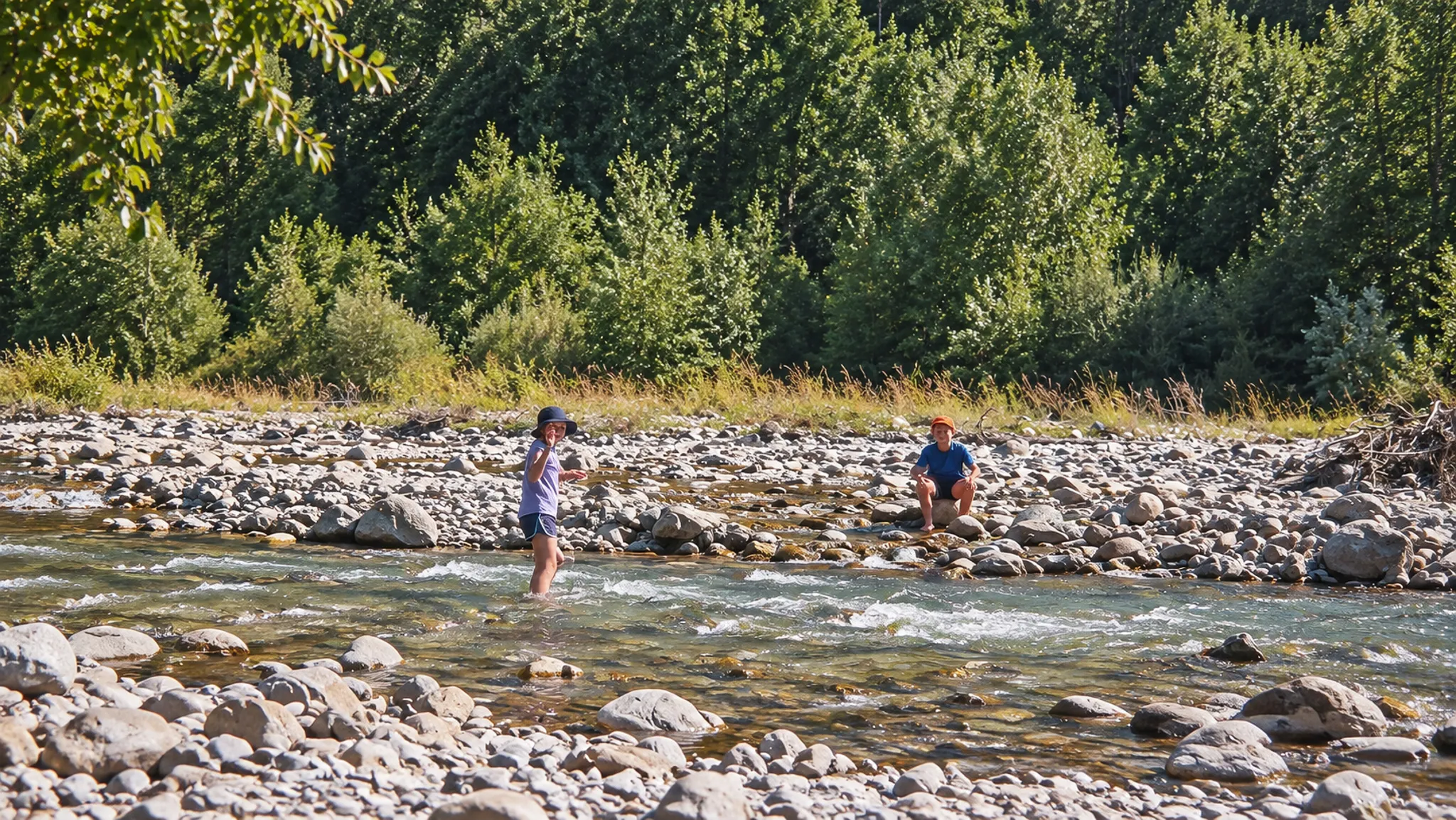 Deux personnes dans une rivière peu profonde, entourées de galets et de verdure alpine.