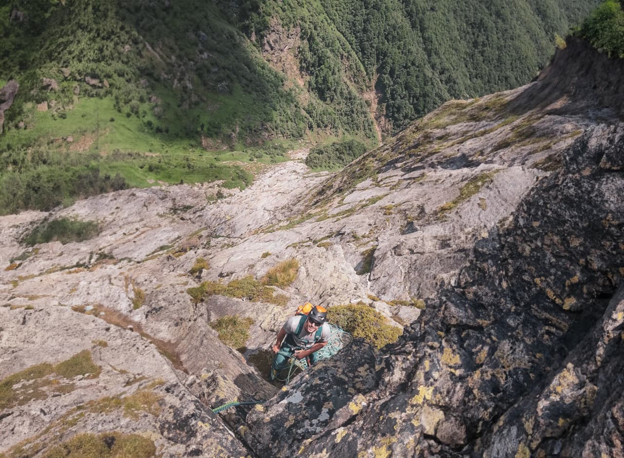 Alpiniste progressant sur un rocher escarpé, surplombant des paysages verdoyants des Pyrénées.