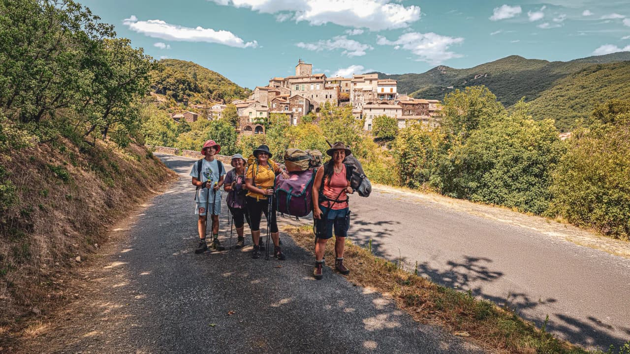 A happy group of hikers with a donkey, in front of a picturesque village in the Cévennes.