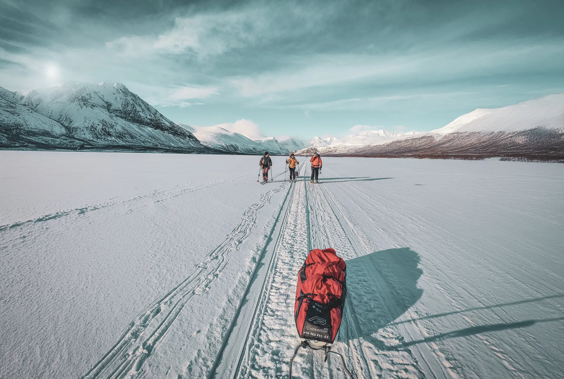 Un groupe d'expédition avance en raquettes sur un lac gelé, entouré de montagnes enneigées.