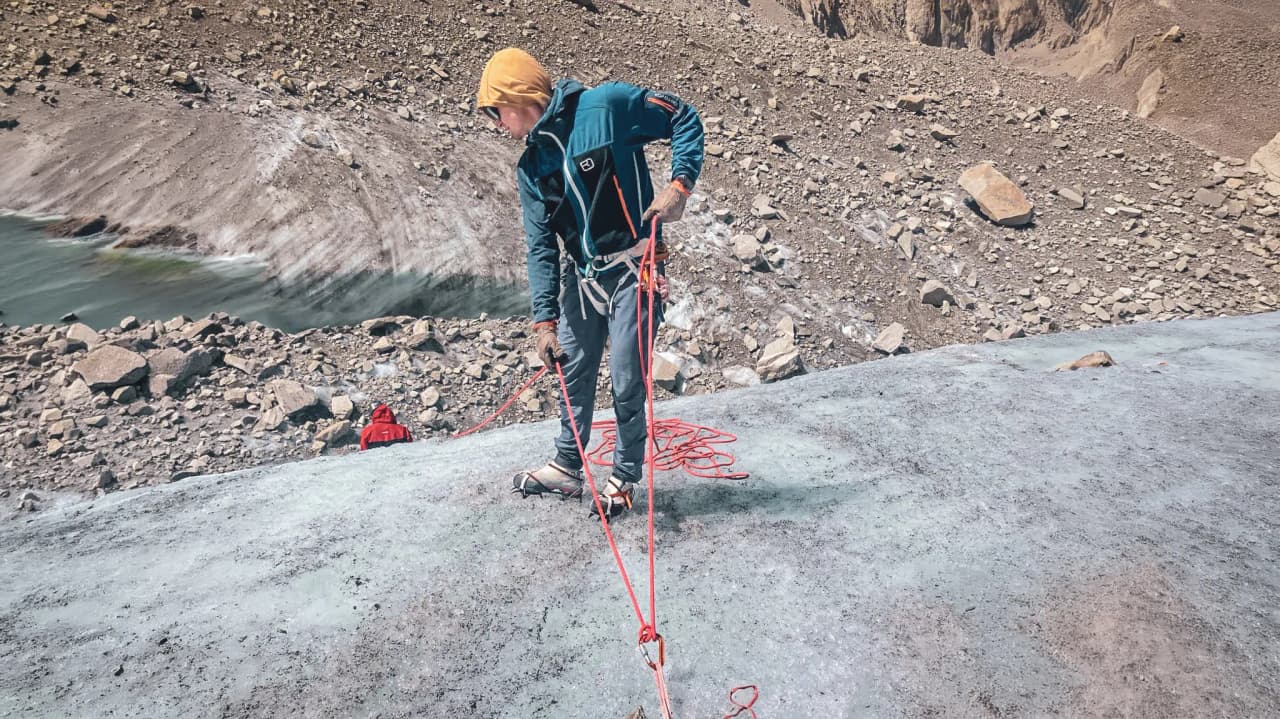Alpiniste sur un glacier, préparant son équipement dans un paysage alpin à couper le souffle.