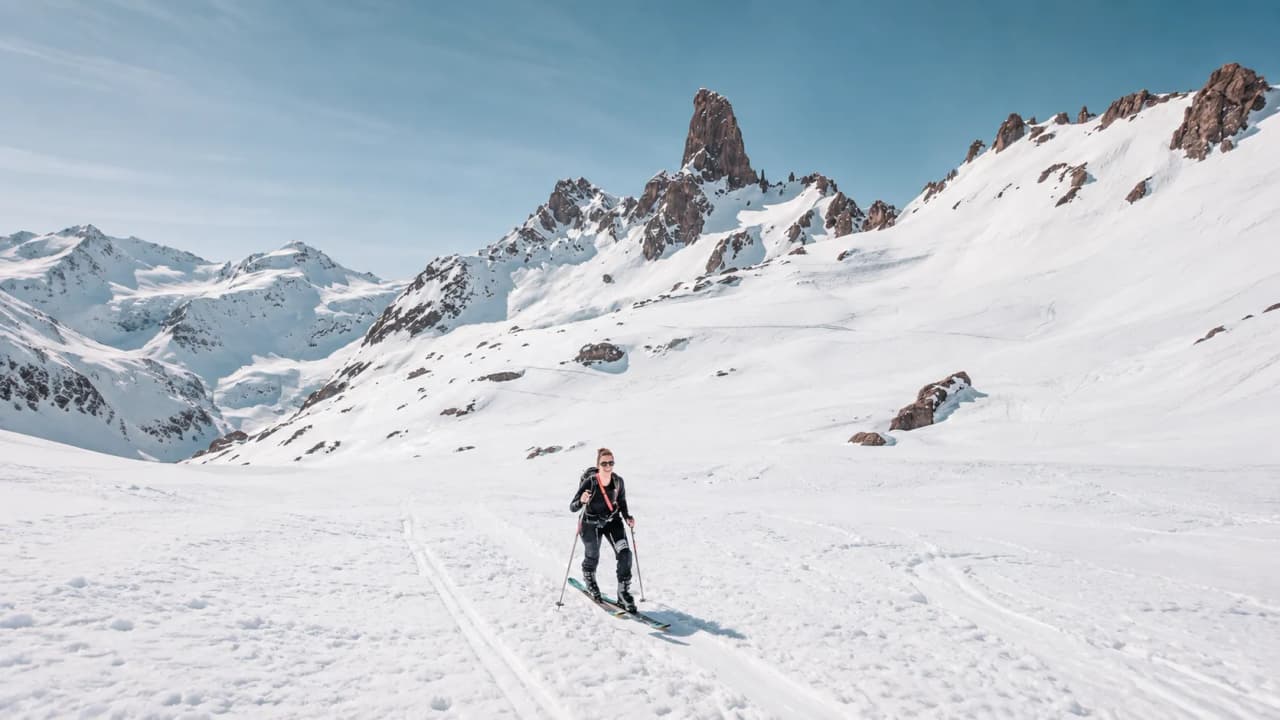 A skier making his way up a slope of pristine snow, with majestic mountains stretching out before him.