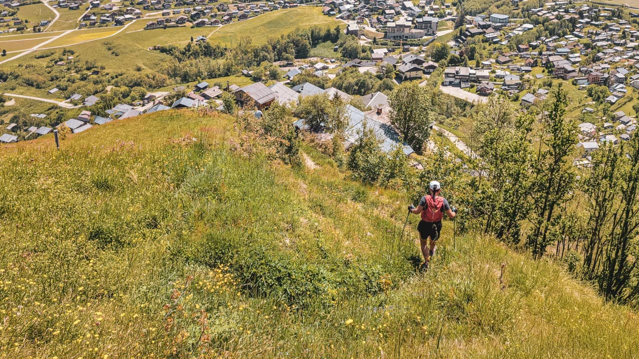 Un coureur traverse un sentier verdoyant, surplombant un village pittoresque en pleine nature.