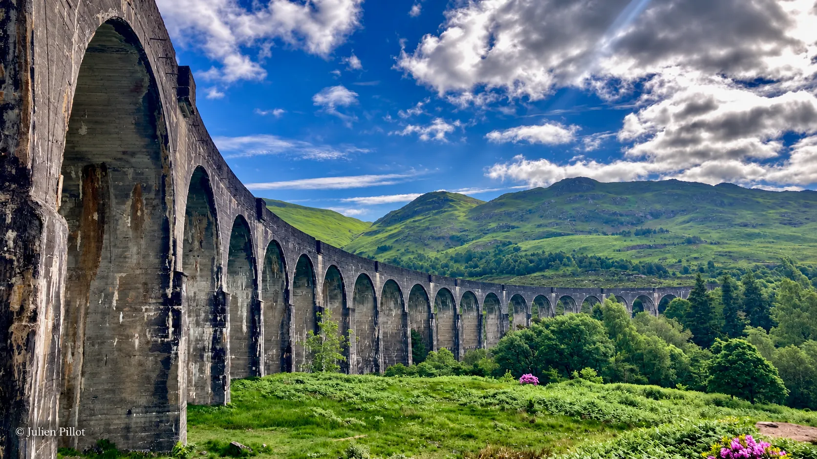 Een majestueus viaduct dat uitkijkt over groene heuvels onder een stralende hemel in Schotland.