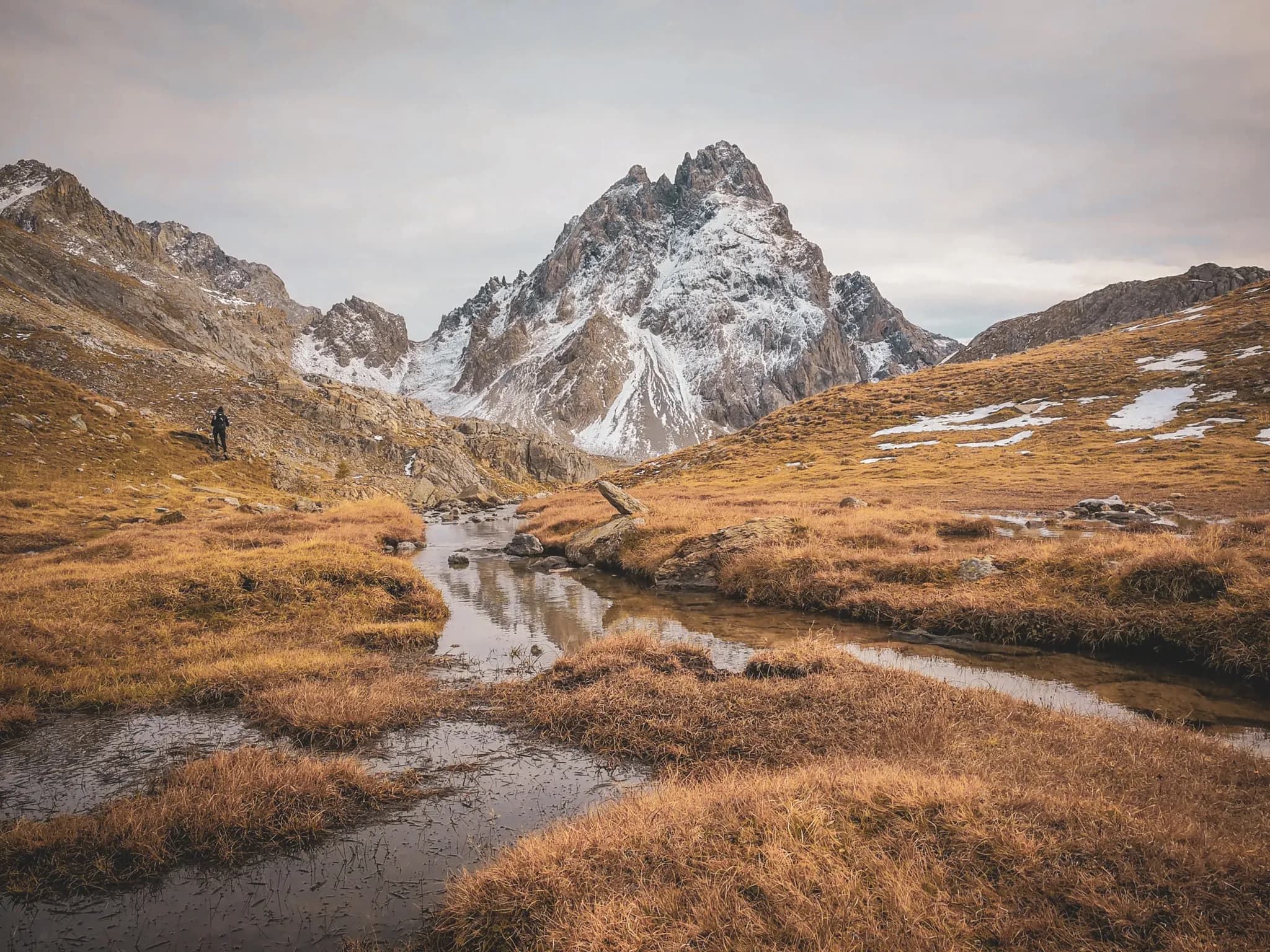 Een wandelaar verkent een wild alpenlandschap, tussen majestueuze bergen en een vredig beekje.