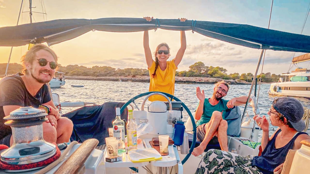 A group of smiling people are relaxing on a sailing boat, enjoying the sunset in the Balearic Islands.