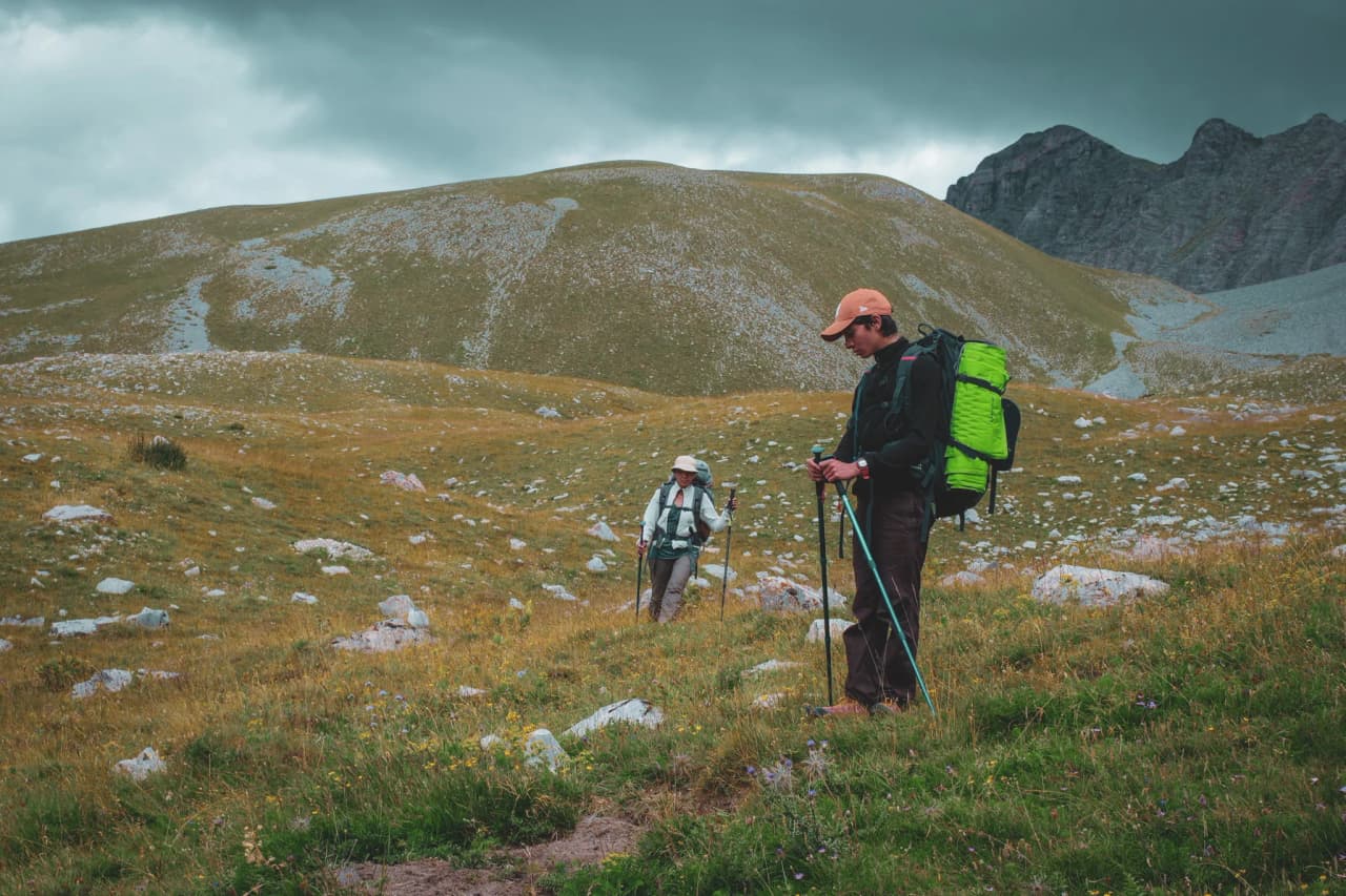Two hikers explore the vast meadows of the Vercors, surrounded by majestic mountains.