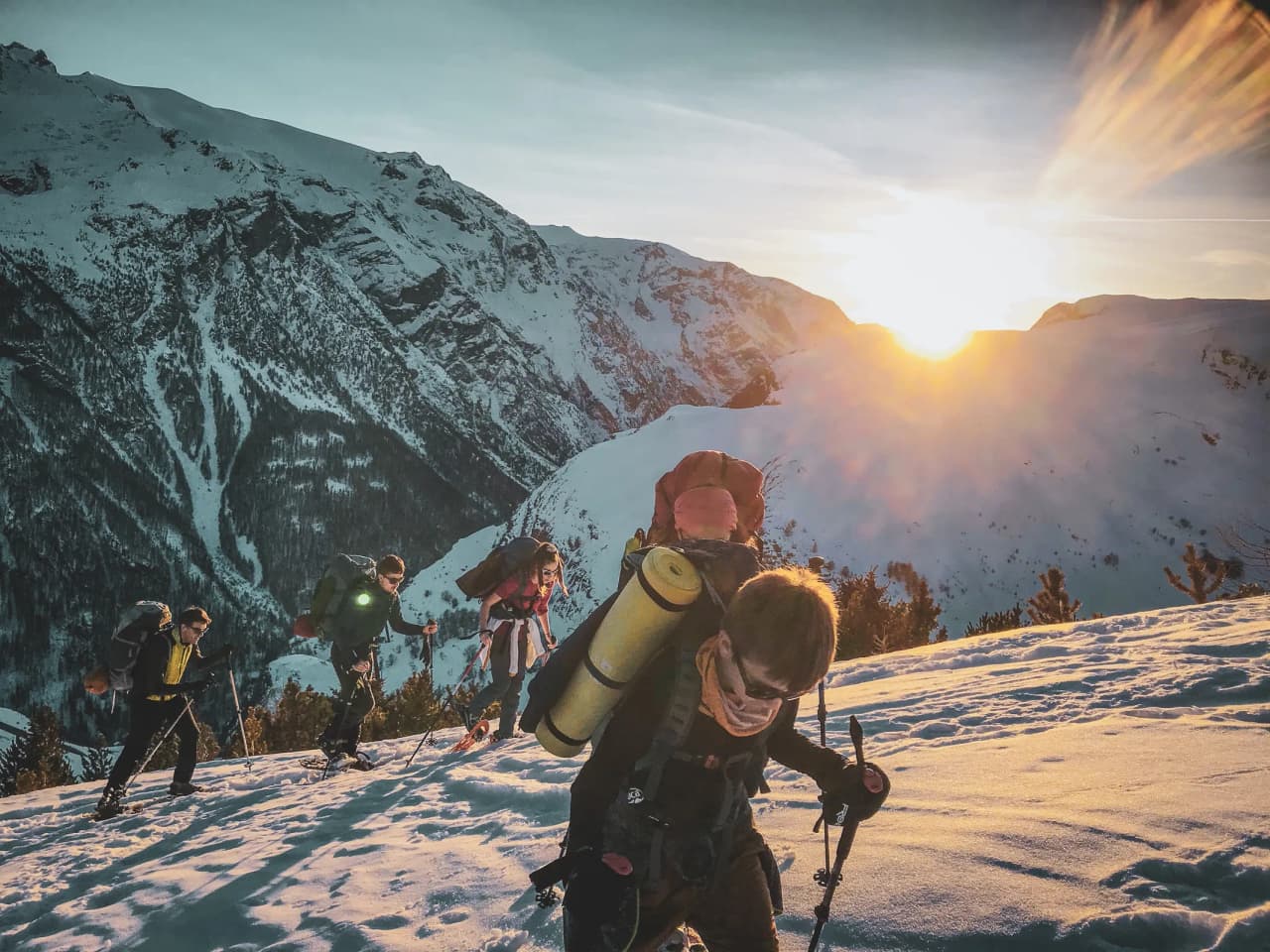 Groupe d'amis en raquettes, escaladant des montagnes enneigées au coucher du soleil.