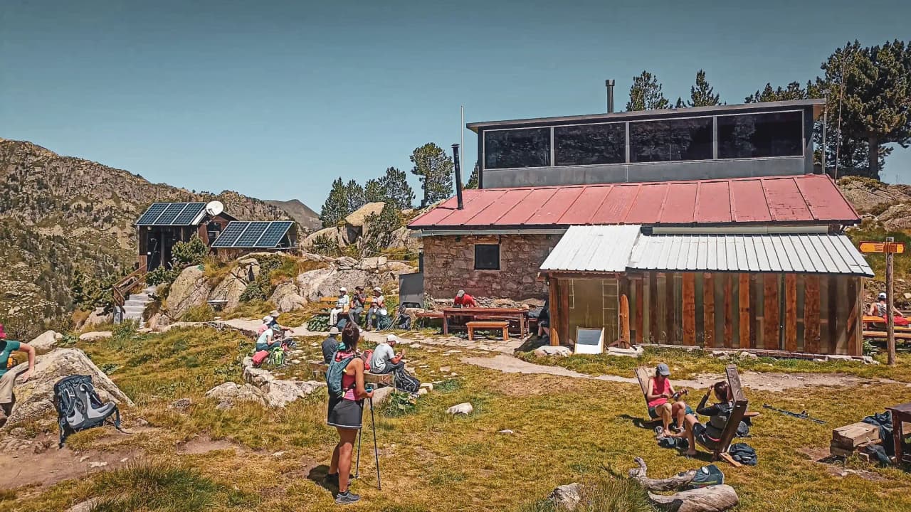 Mountain hut surrounded by lush green countryside and hikers soaking up the sun.