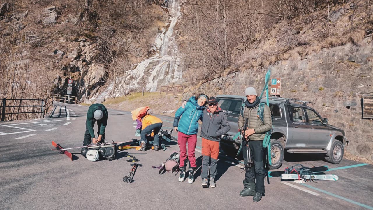 Groupe joyeux préparant une expédition de ski au Mont Viso, avec paysages alpins en arrière-plan.
