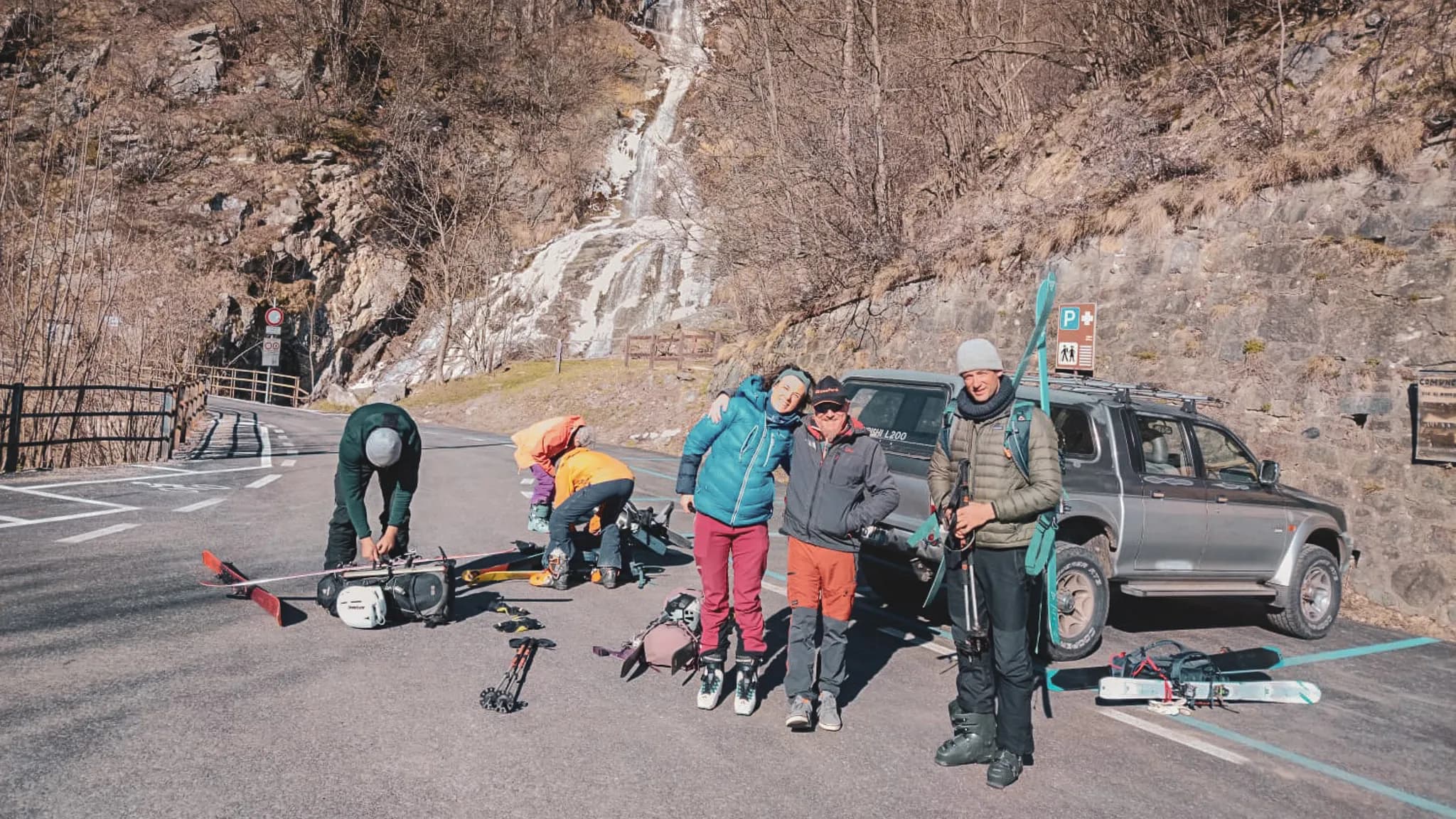 Groupe joyeux préparant une expédition de ski au Mont Viso, avec paysages alpins en arrière-plan.