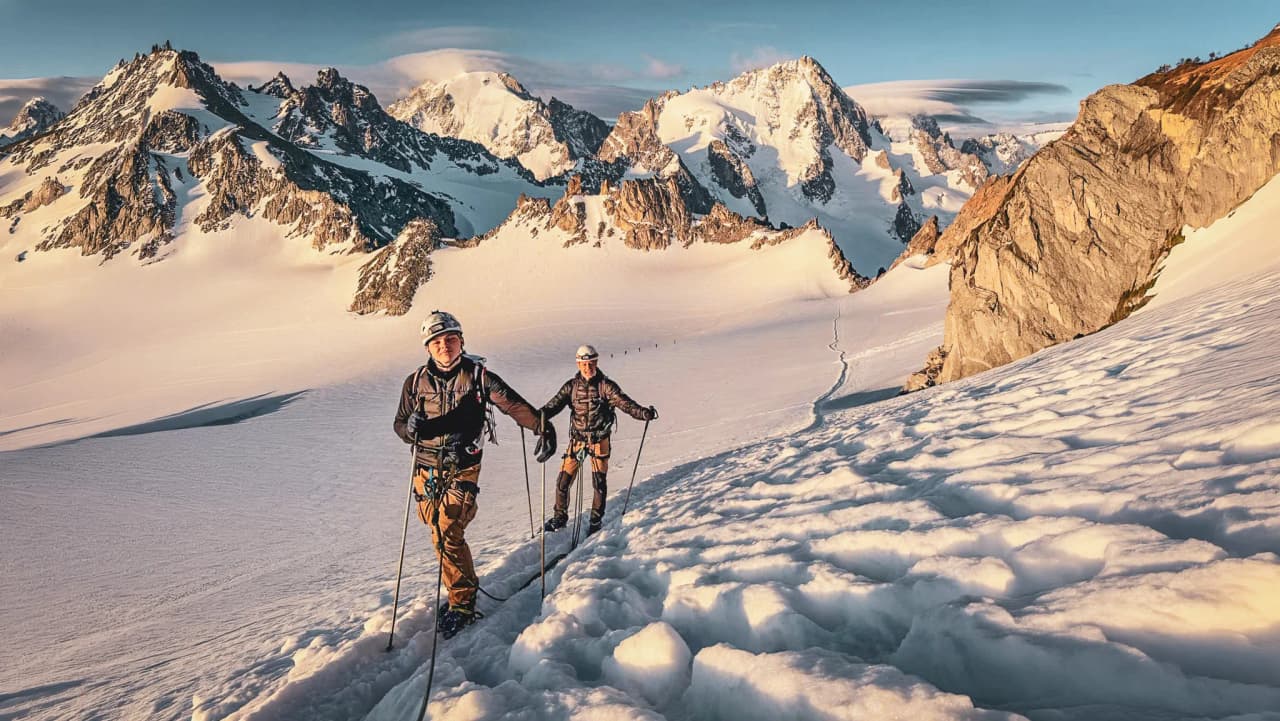 Mountaineers on a glacier, with majestic peaks in the background at sunrise.