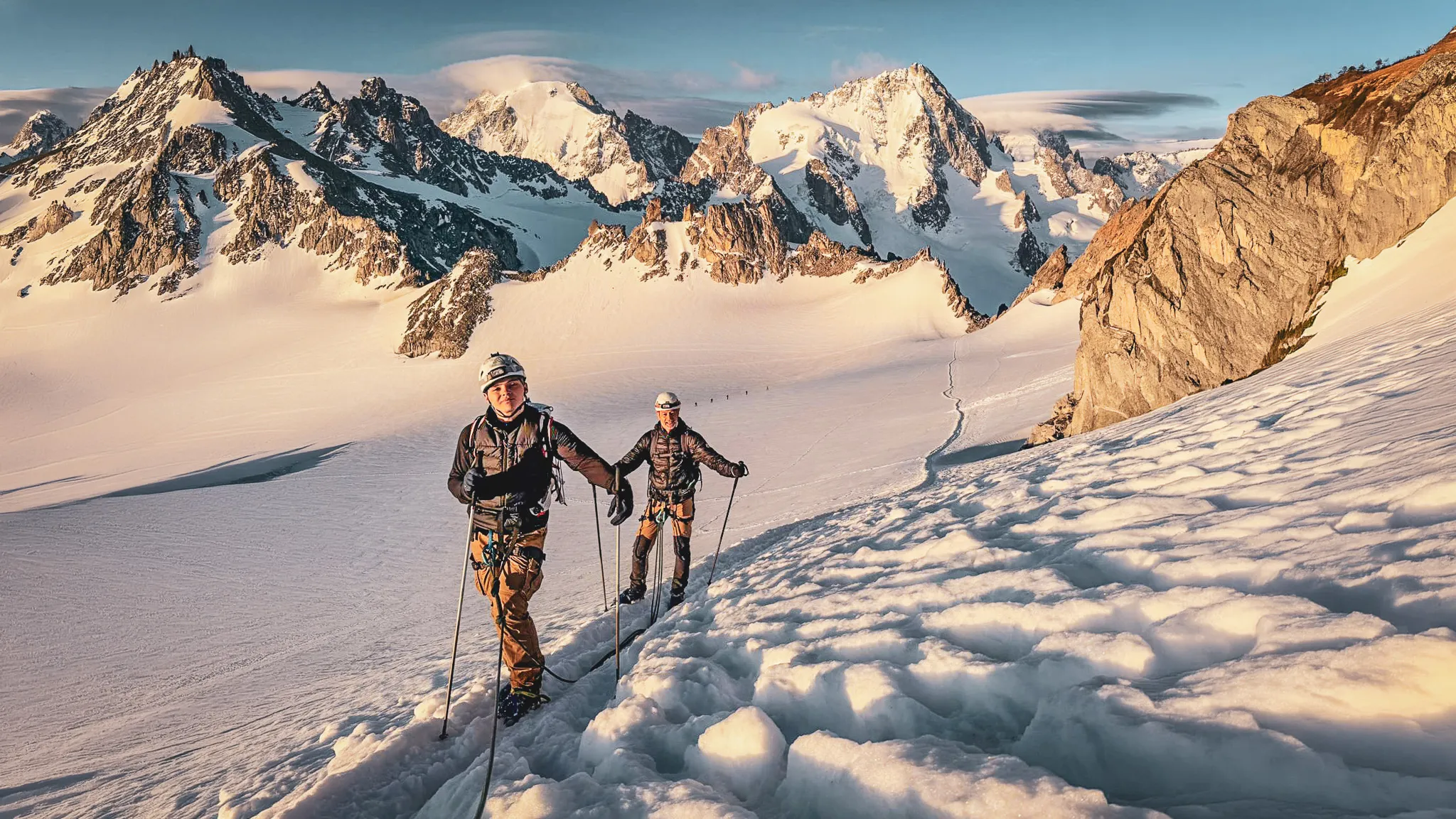 Alpinistes sur un glacier, avec des sommets majestueux en arrière-plan au lever du soleil.